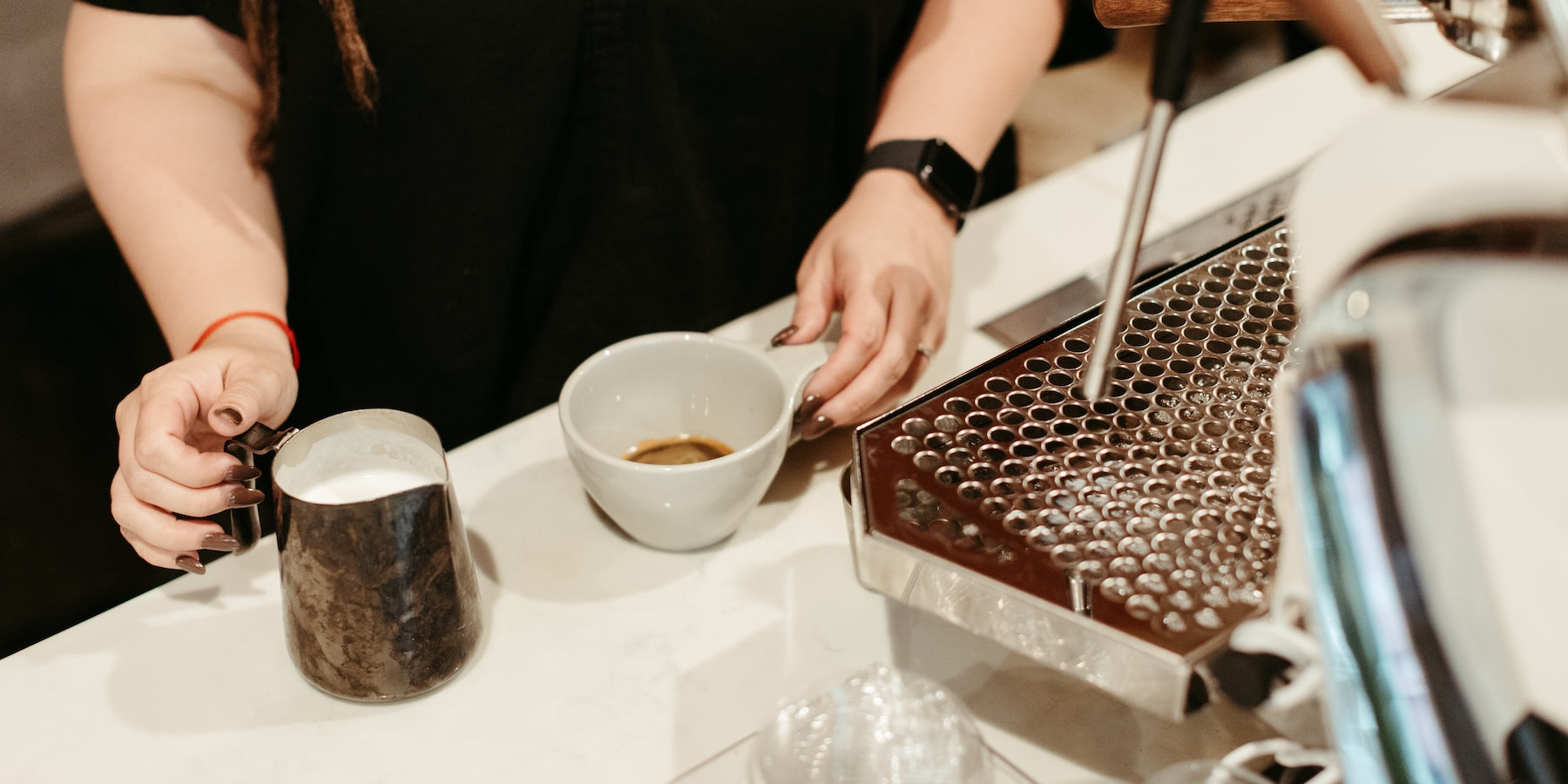 photograph of hands holding a pitcher of steamed milk and a shot of espresso