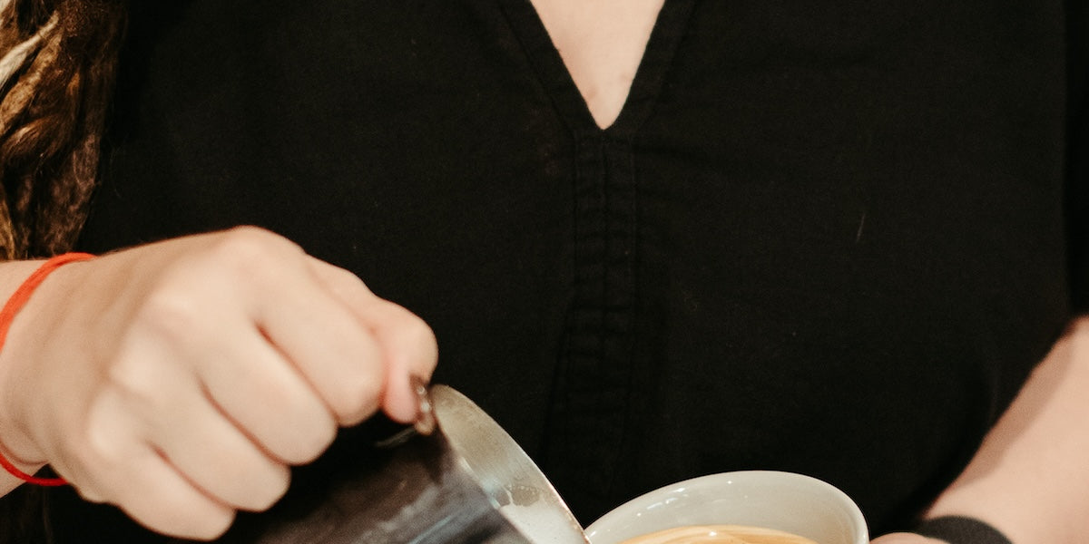 photograph of a woman pouring stemed milk into a cup of espresso