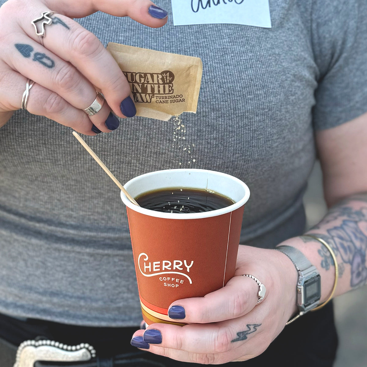woman holding cherry coffee shop to-go cup sprinkling sugar in the raw in it.
