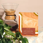 photograph of Cherry Coffee's Half-Caff blend, next to a Chemex filled with coffee and a plant