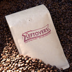 photograph of a craft bag filled with 'the leftovers fine scrap coffee' in a sea of coffee beans