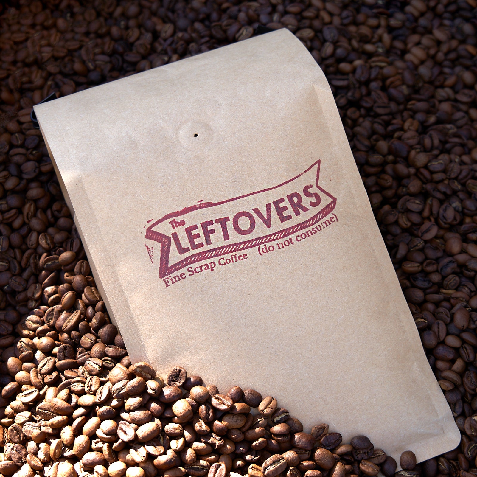 photograph of a craft bag filled with 'the leftovers fine scrap coffee' in a sea of coffee beans