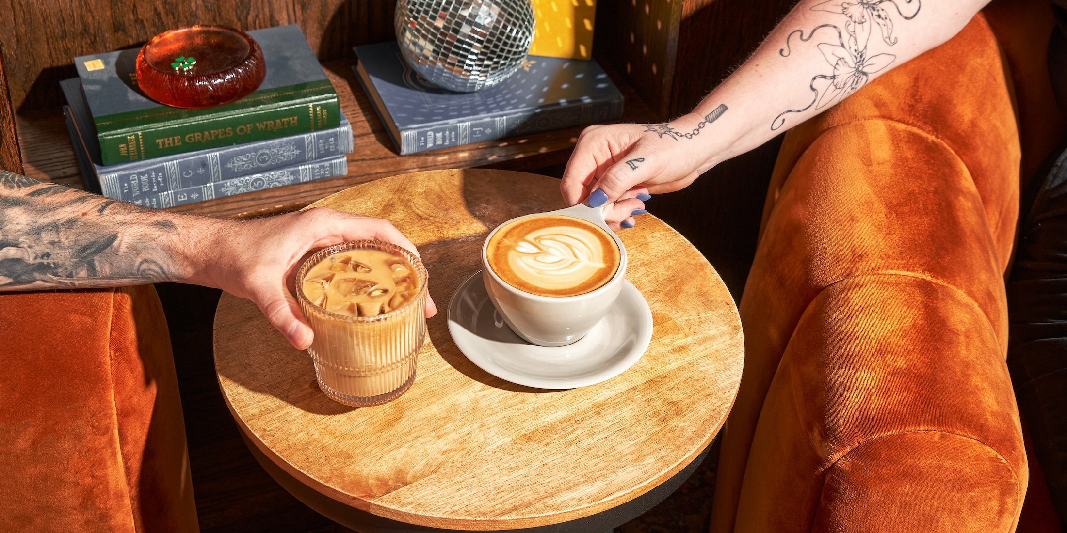 photograph of two arms grabbing an iced and hot coffee drink at cherry coffee shop
